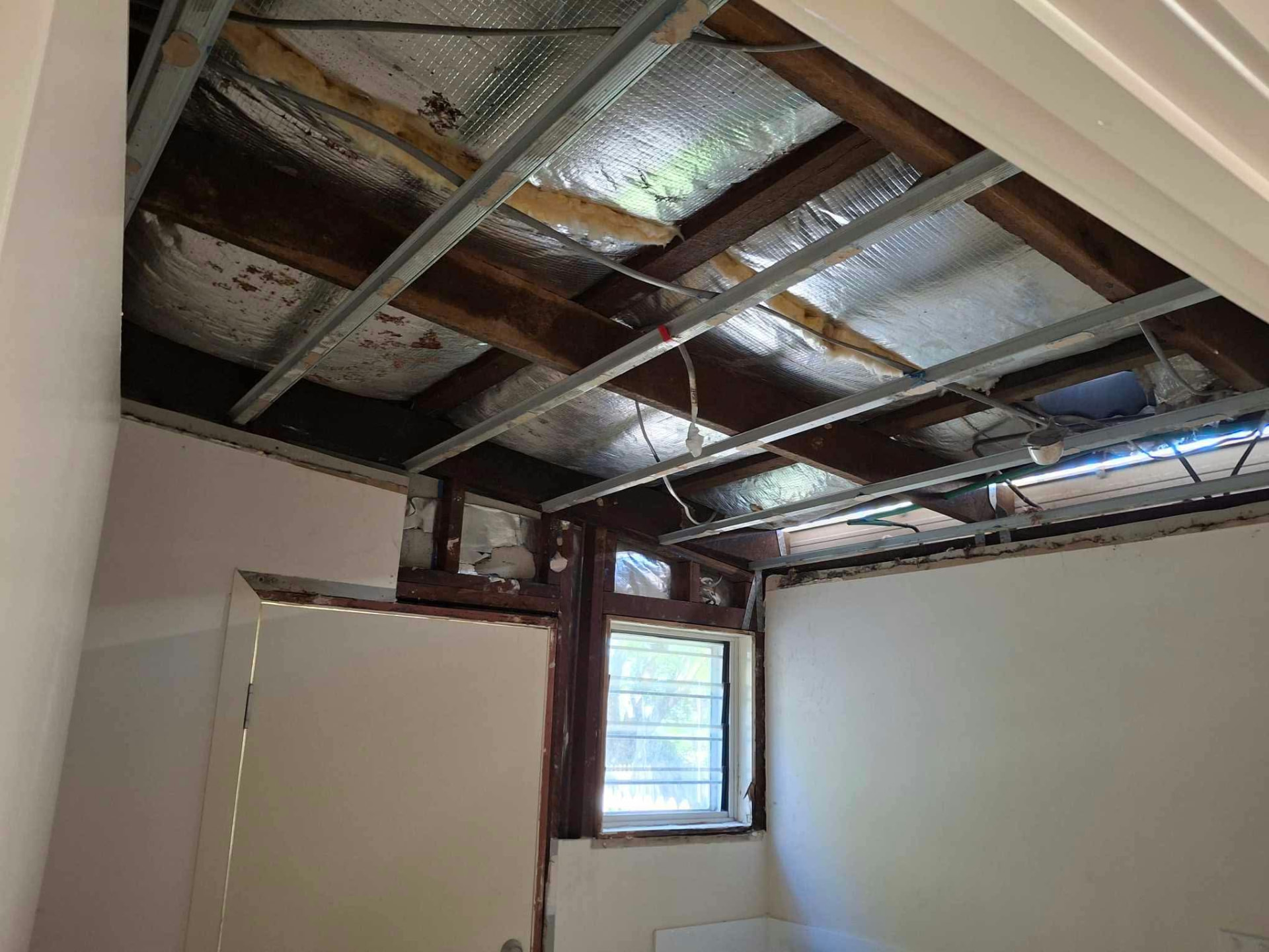Ceiling lining removed to expose timber joists, steel battens and insulation above a plasterboard wall
