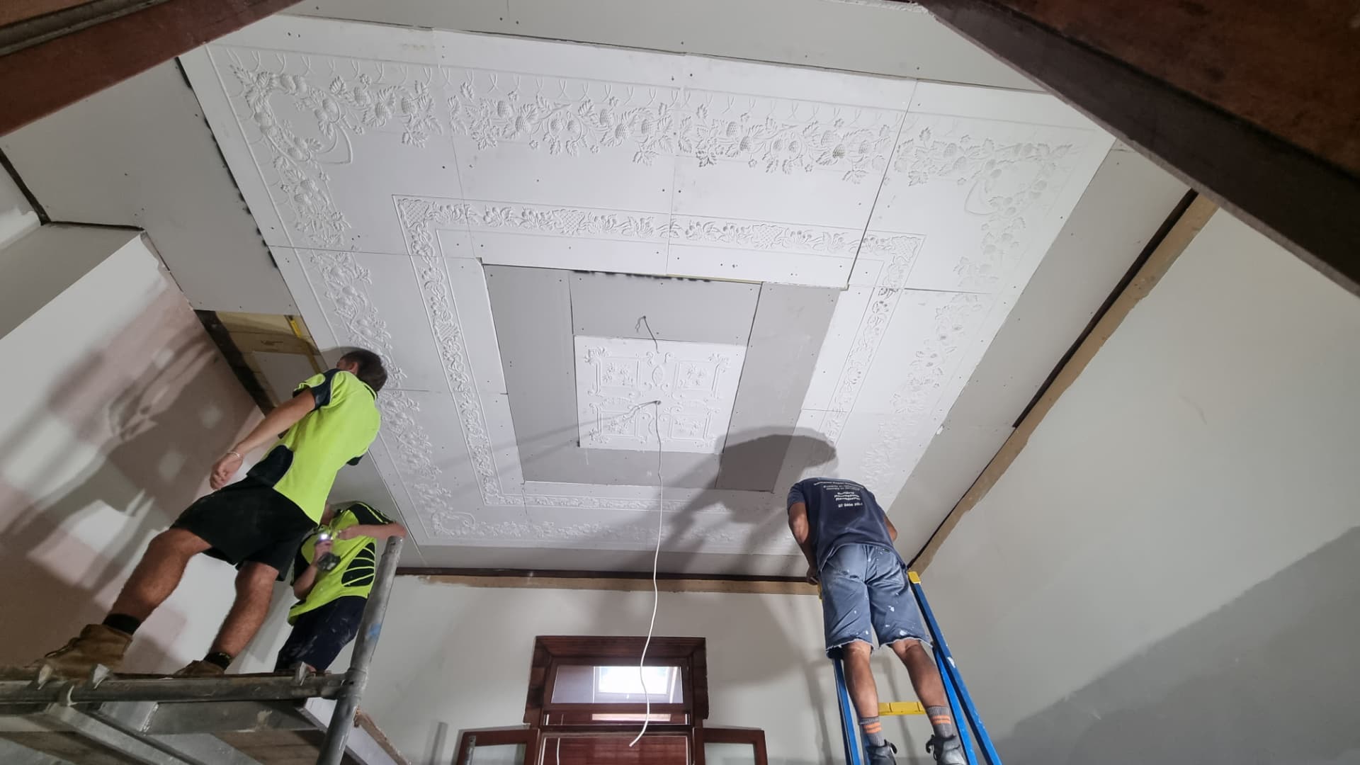 Workers fitting a decorative ceiling panel on a renovation project